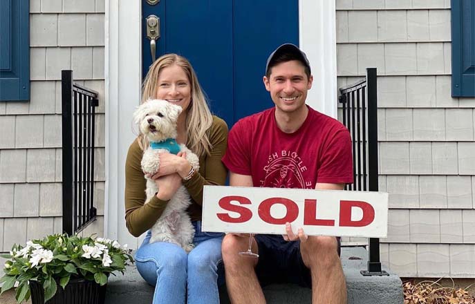 Couple on front porch with sold sign and dog